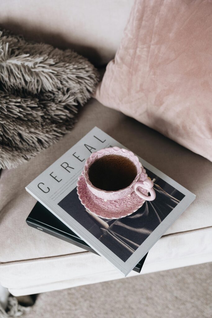 A pink ceramic mug on top of a fashionable magazine in a cozy setting, perfect for relaxation.