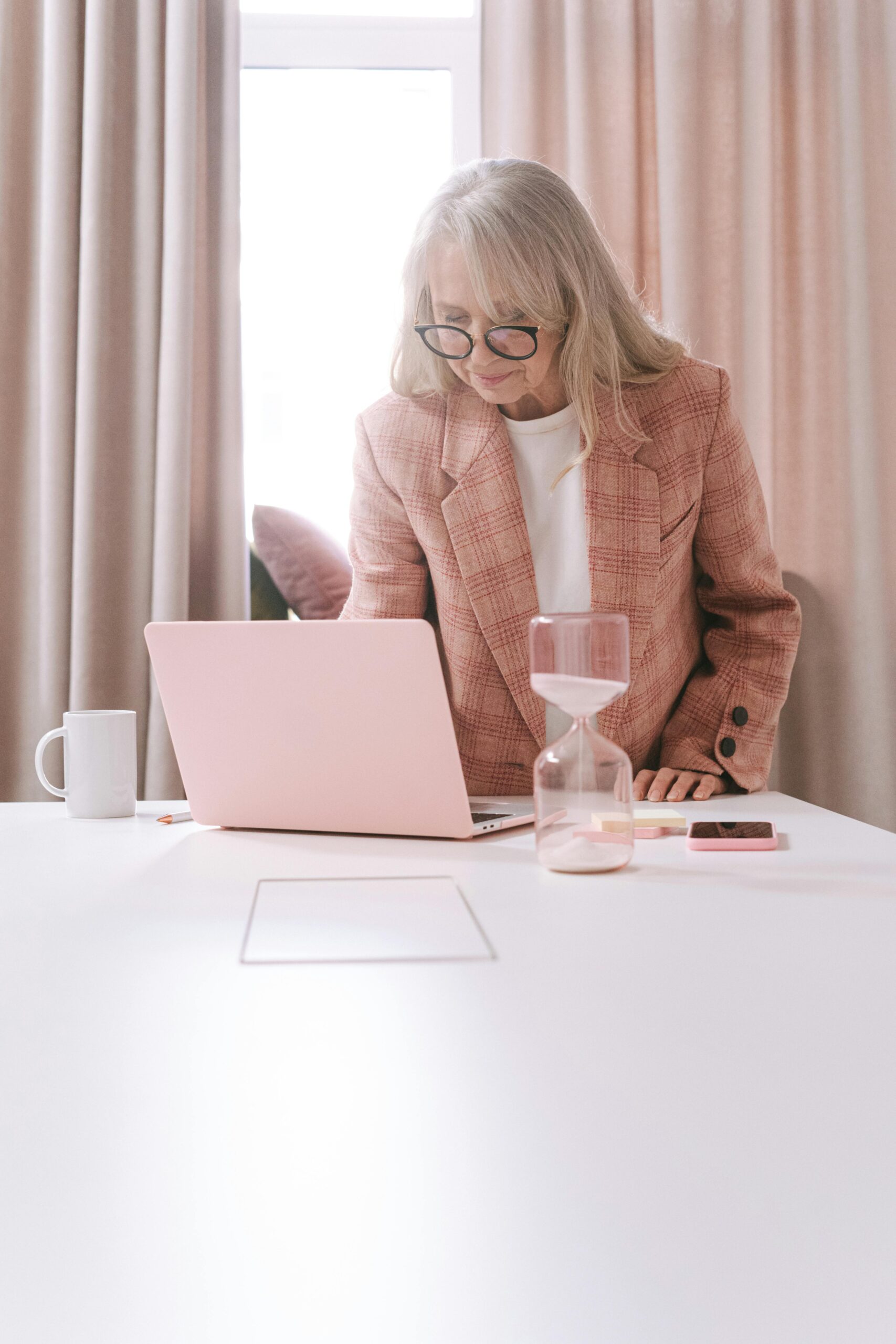 A focused senior woman works on her laptop at a modern home office desk.
