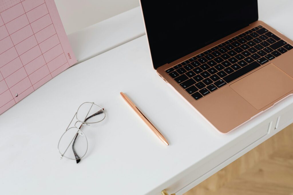 A clean and organized workspace with a laptop, planner, glasses, and pen on a desk.